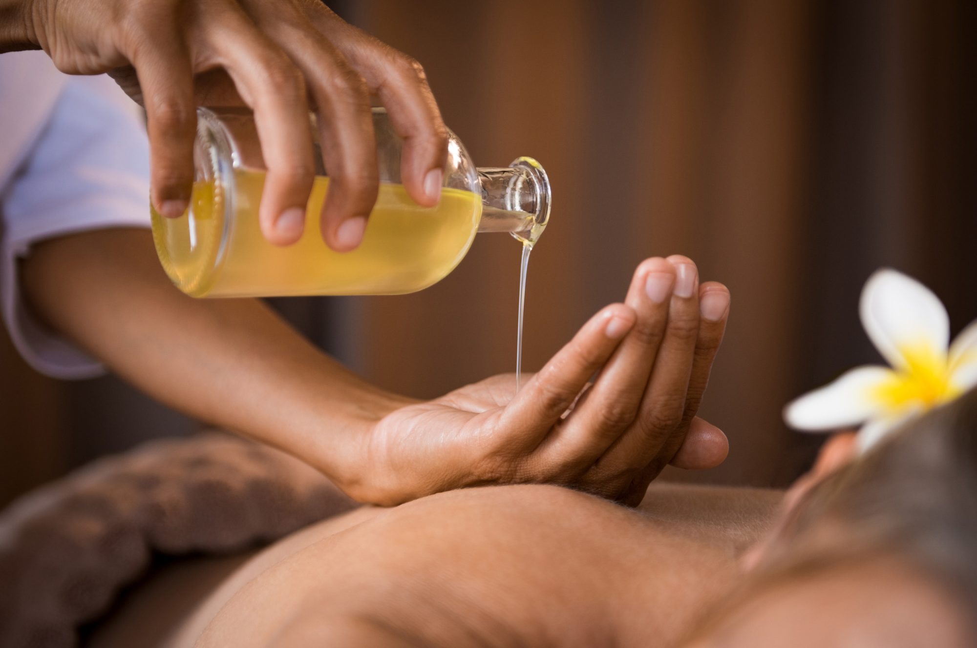 Therapist pouring massage oil at spa. Closeup of masseur hands pouring aroma oil on women back. Masseuse prepare to do oriental spa procedure for relaxing treatment. Therapist doing aromatherapy oil massage on women body.